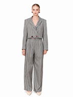 A model wearing a gray pinstripe double-breasted jumpsuit with wide-leg trousers, styled with beige pointed-toe heels against a plain white background.