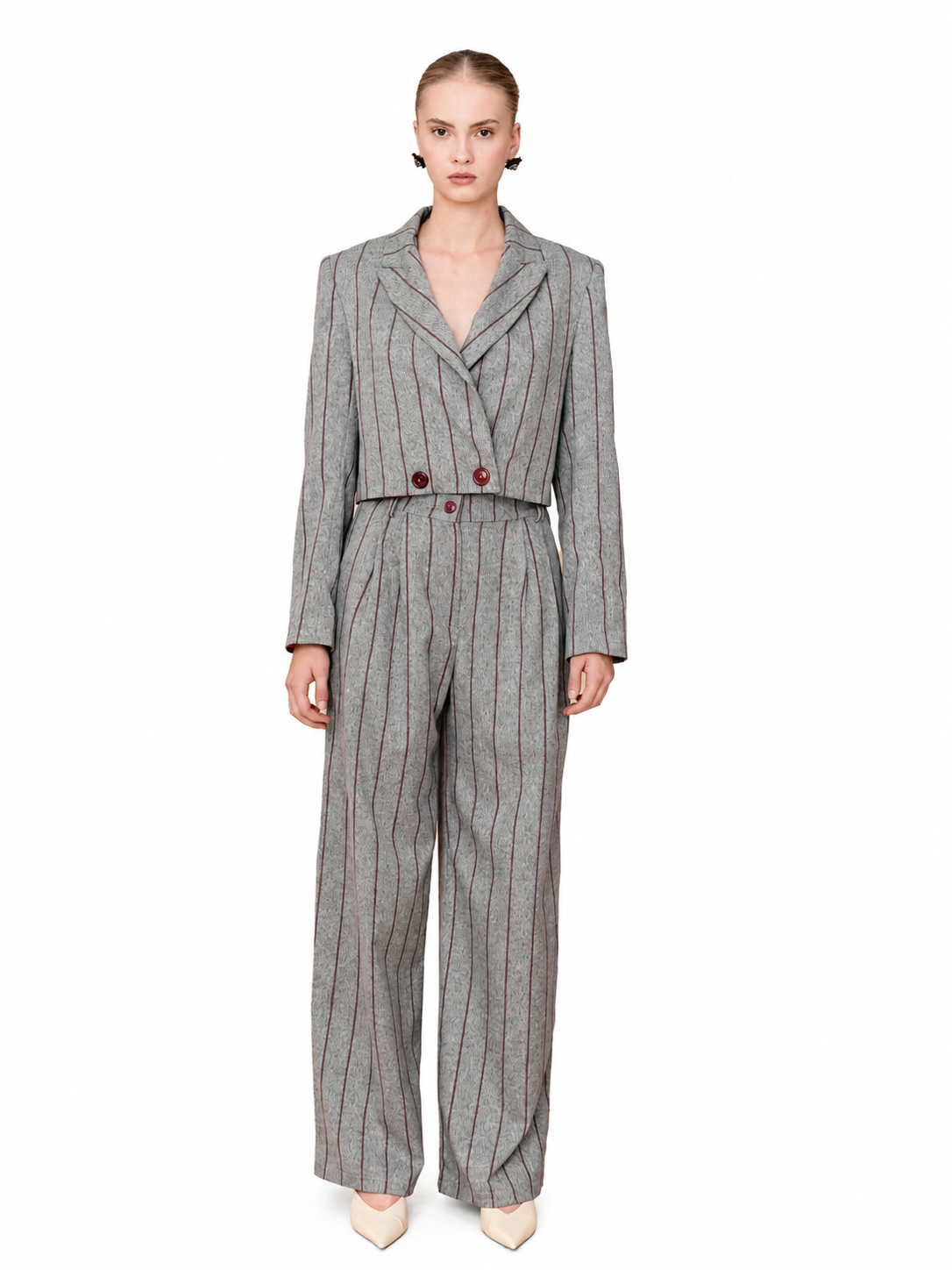 A model wearing a gray pinstripe double-breasted jumpsuit with wide-leg trousers, styled with beige pointed-toe heels against a plain white background.