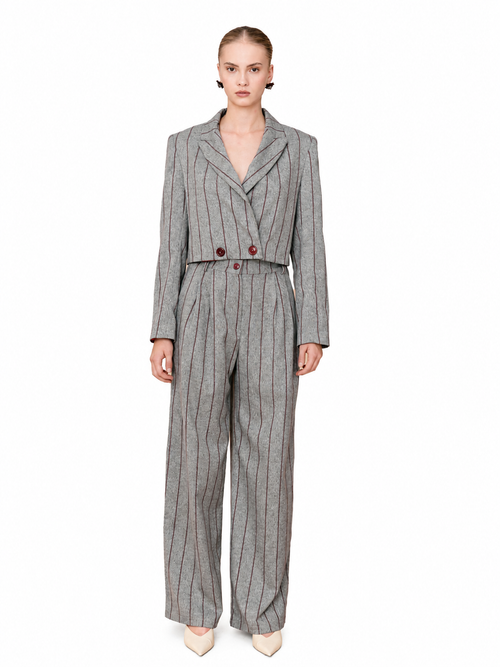 A model wearing a gray pinstripe double-breasted jumpsuit with wide-leg trousers, styled with beige pointed-toe heels against a plain white background.