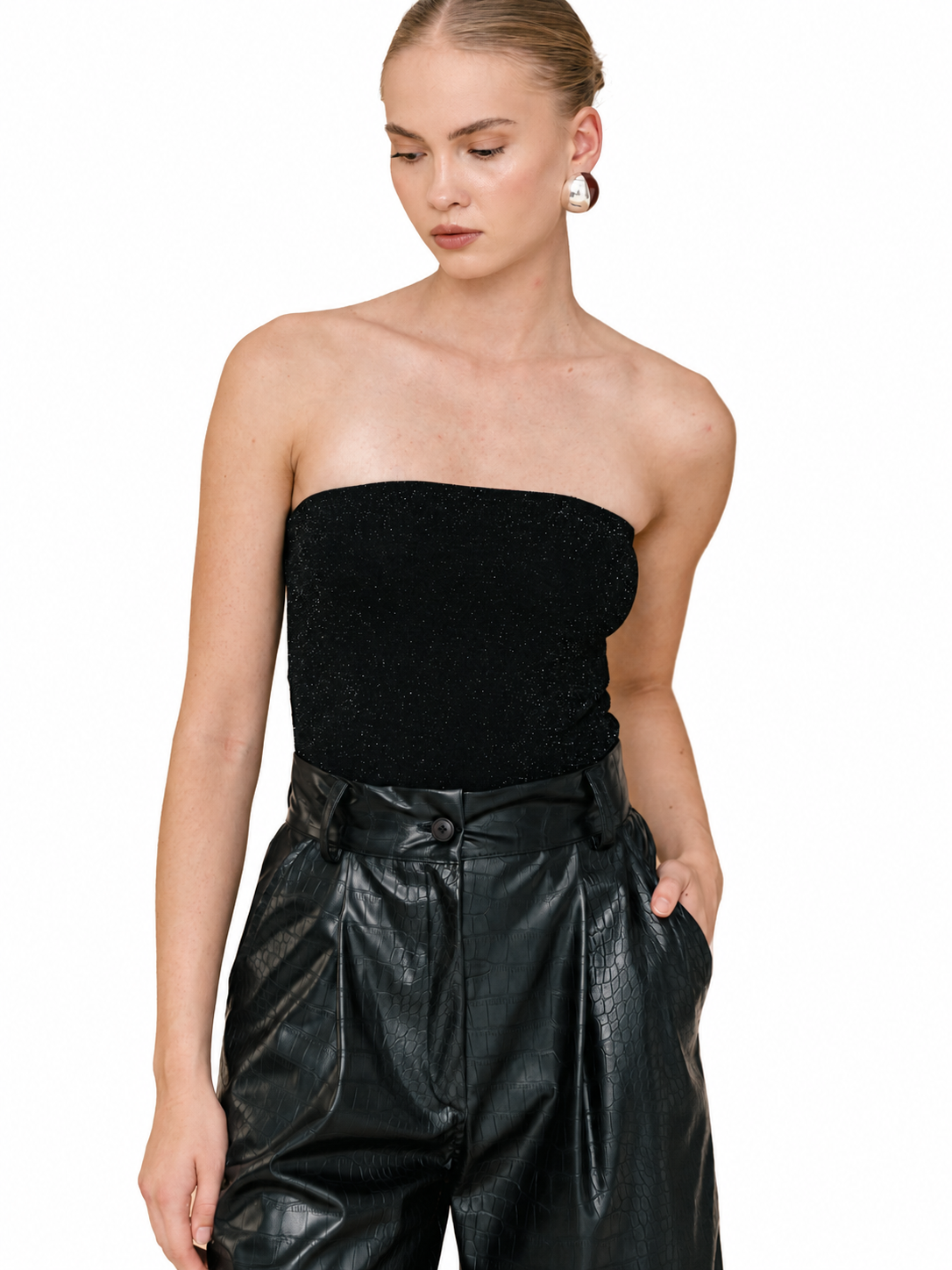 A woman modeling a black strapless textured tube top paired with black faux-leather trousers, shown against a plain white background.