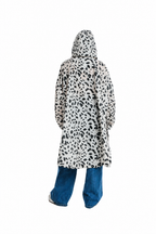 A person shown from the back wearing a hooded long coat with a black irregular spotted pattern on a white base, paired with blue jeans, against a plain white background.