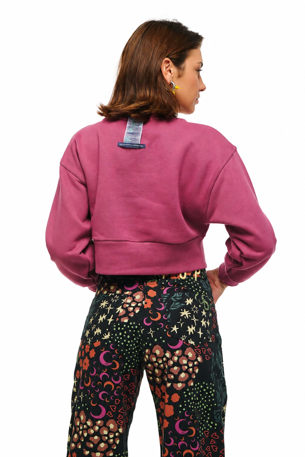 A woman shown from the back wearing a dusty rose cropped sweatshirt and black pants with a colorful psychedelic pattern of stars, moons, and dots.