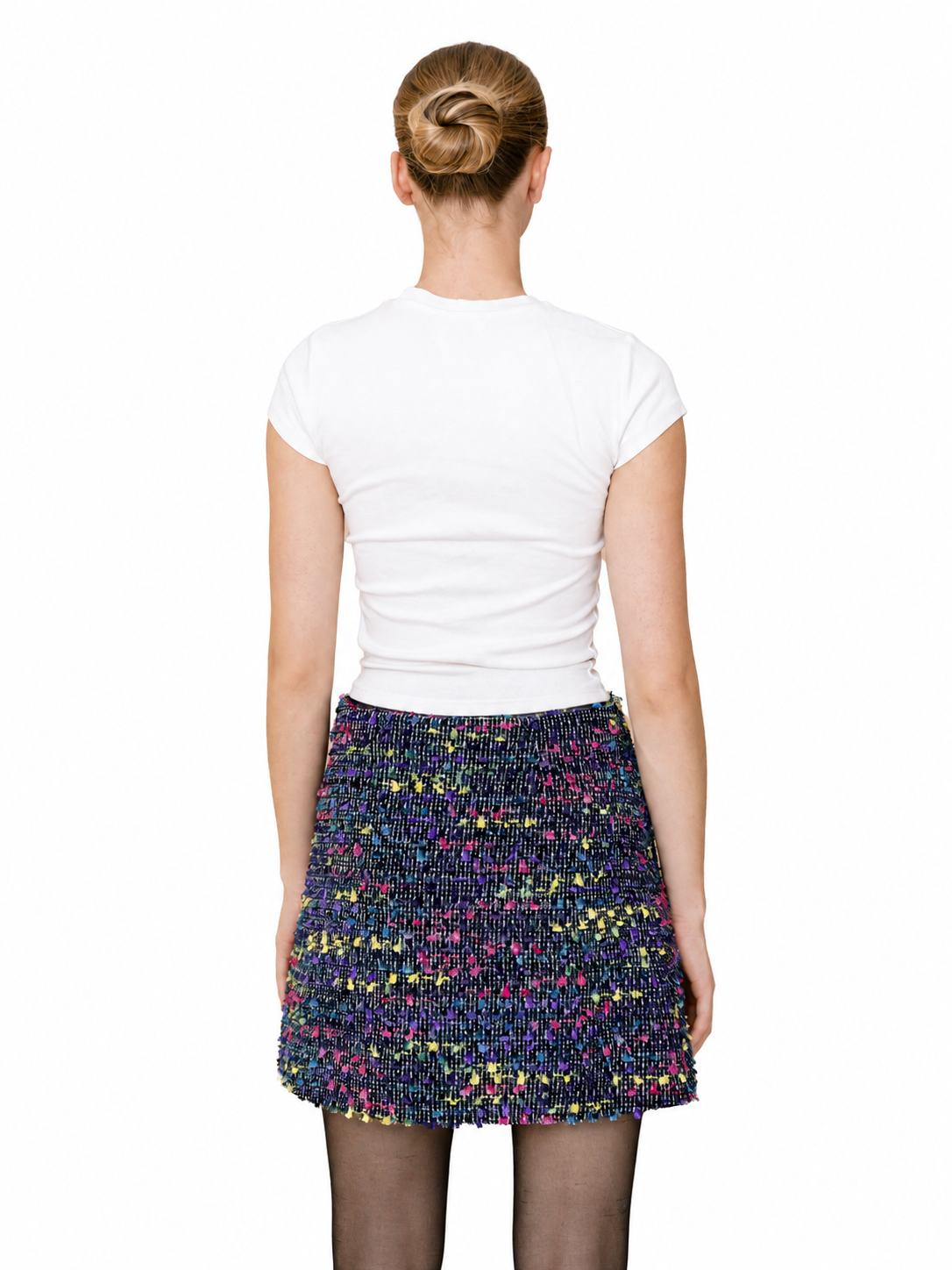 A woman shown from the back wearing a white short-sleeve top and a multicolor tweed mini skirt against a plain white background.