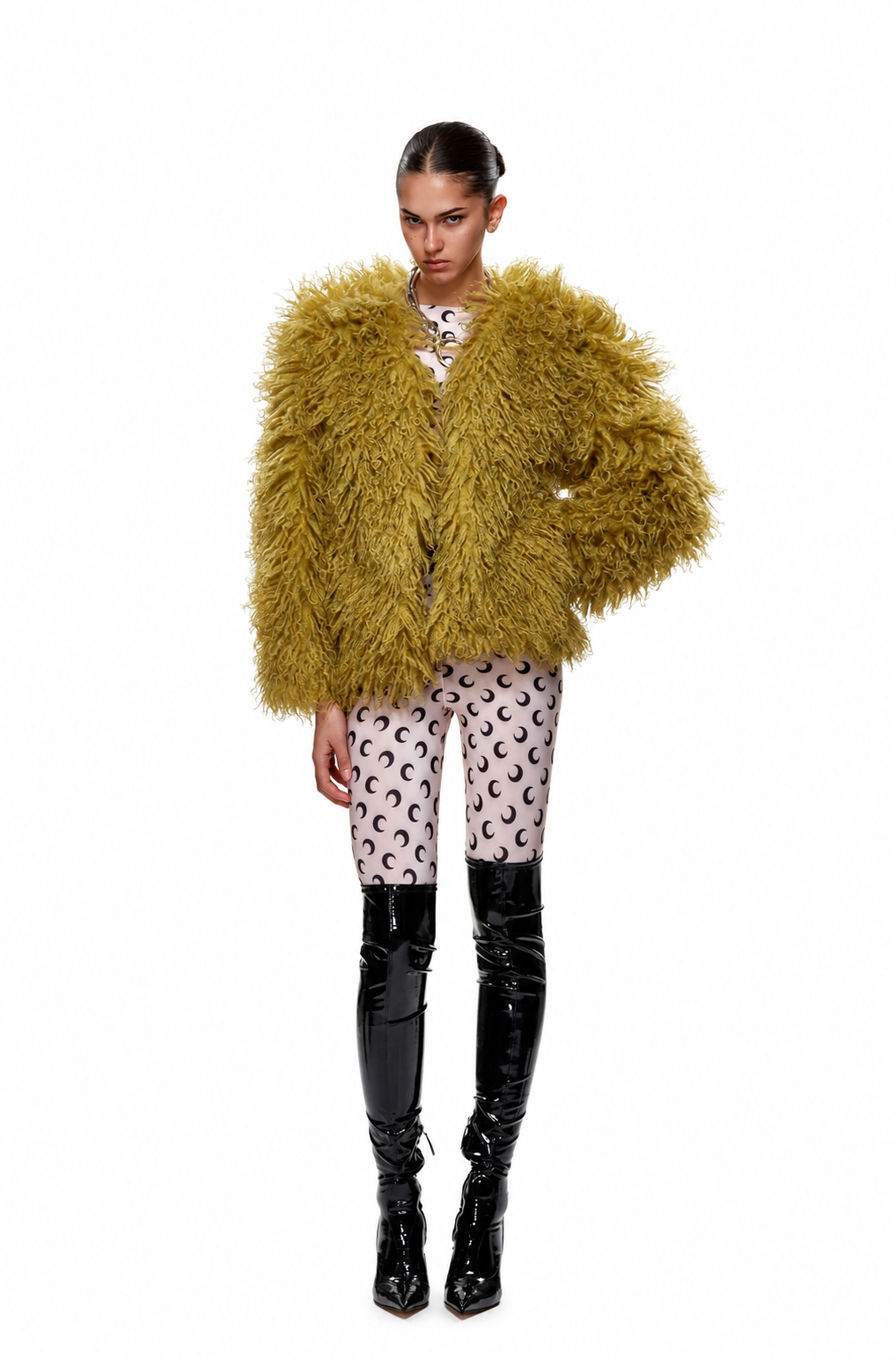 A model wearing a chunky, shaggy olive-yellow jacket, patterned pink and white leggings, and glossy black patent boots, photographed against a solid white background.