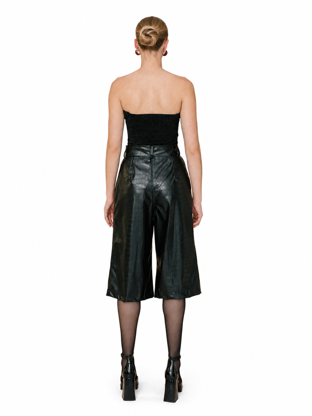 A model shown from the back wearing a black strapless bandeau top and shiny black faux-leather cropped wide-leg pants, paired with sheer black tights and black platform ankle boots, against a plain white background.