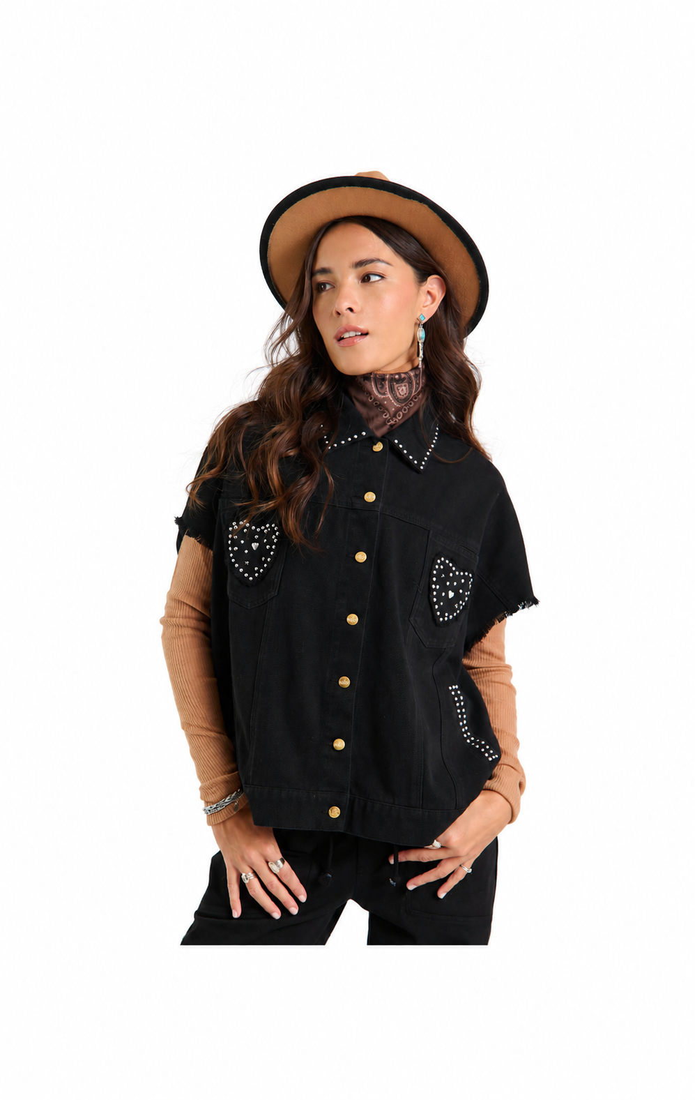 A woman modeling a black western-style denim vest with gold buttons, studded heart pocket details, and frayed sleeves, paired with a tan hat, tan long-sleeve shirt, and black pants against a white background.