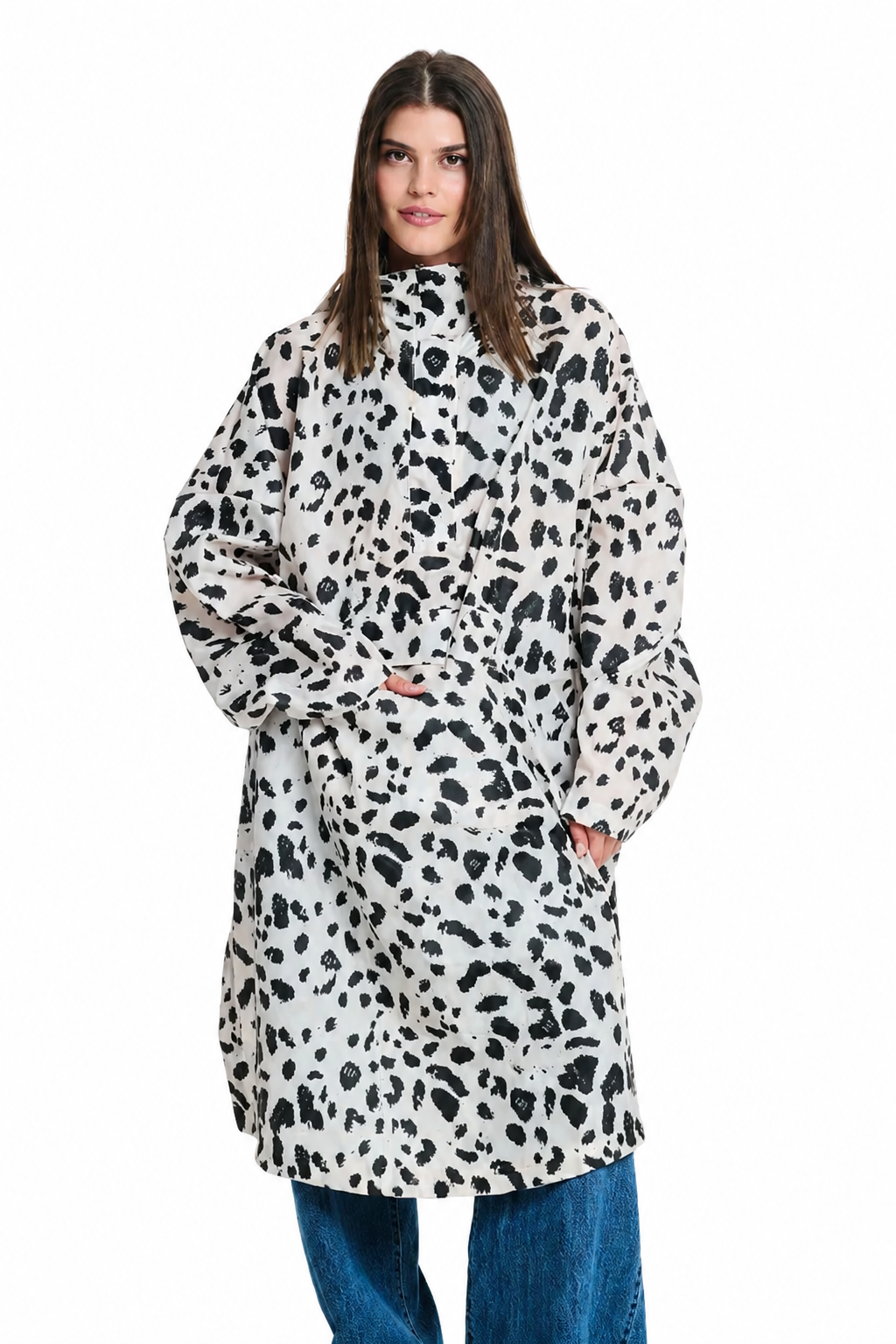 A woman modeling a long-sleeved, high-neck coat with an all-over black and white cow print pattern, paired with blue jeans, against a plain white background.