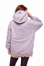 A person shown from the back wearing an oversized light lavender hoodie, with dark leggings and a light pink undershirt visible, against a plain white background.