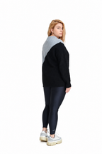 A woman shown from the back wearing a color-block knit sweater with a black body and a light gray shoulder yoke, paired with dark leggings and white platform sneakers, against a plain white background.