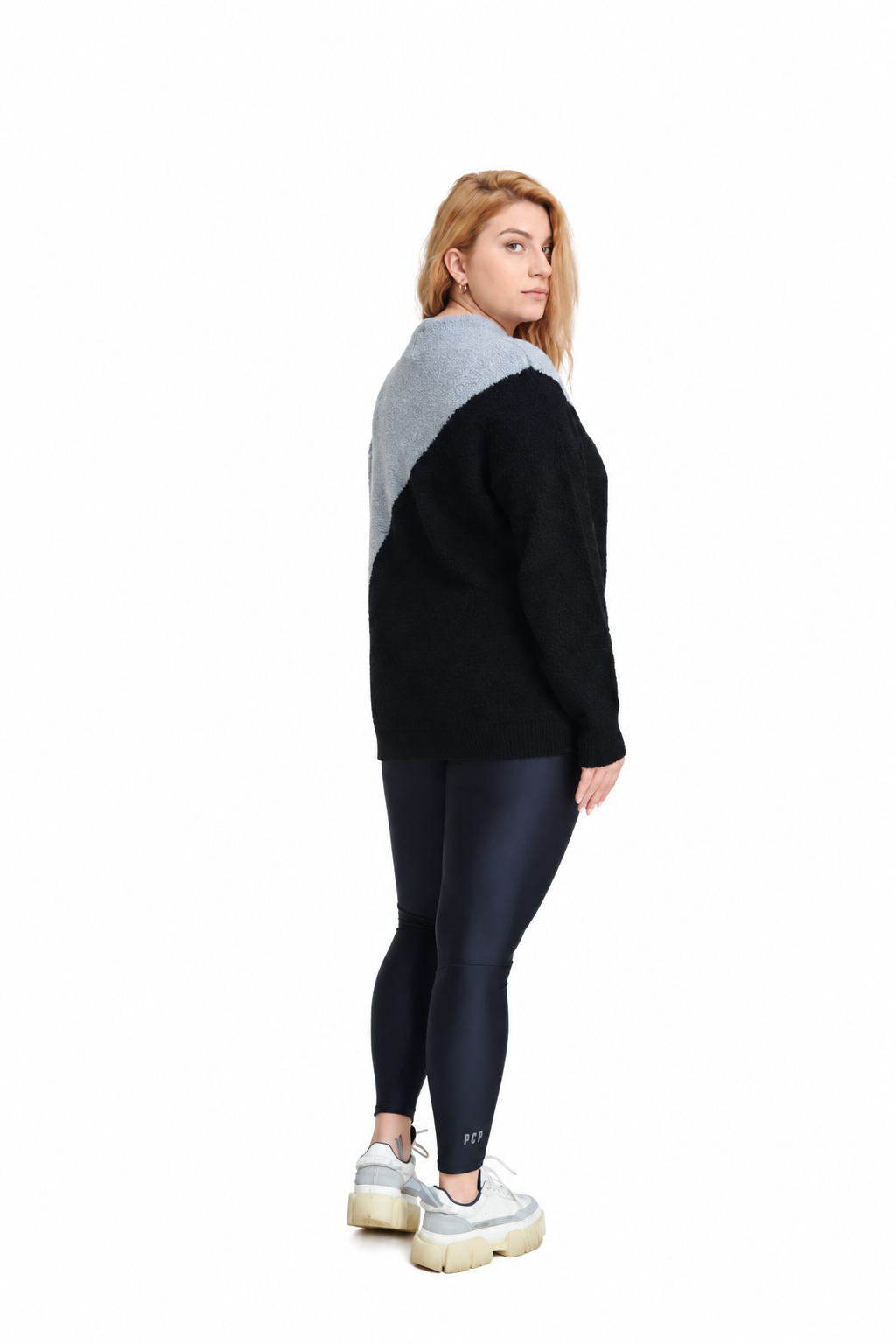A woman shown from the back wearing a color-block knit sweater with a black body and a light gray shoulder yoke, paired with dark leggings and white platform sneakers, against a plain white background.