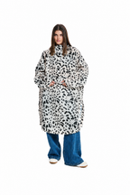 A model wearing a long-sleeved, oversized black and white animal print coat over blue wide-leg jeans and white sneakers, shot against a solid white background.