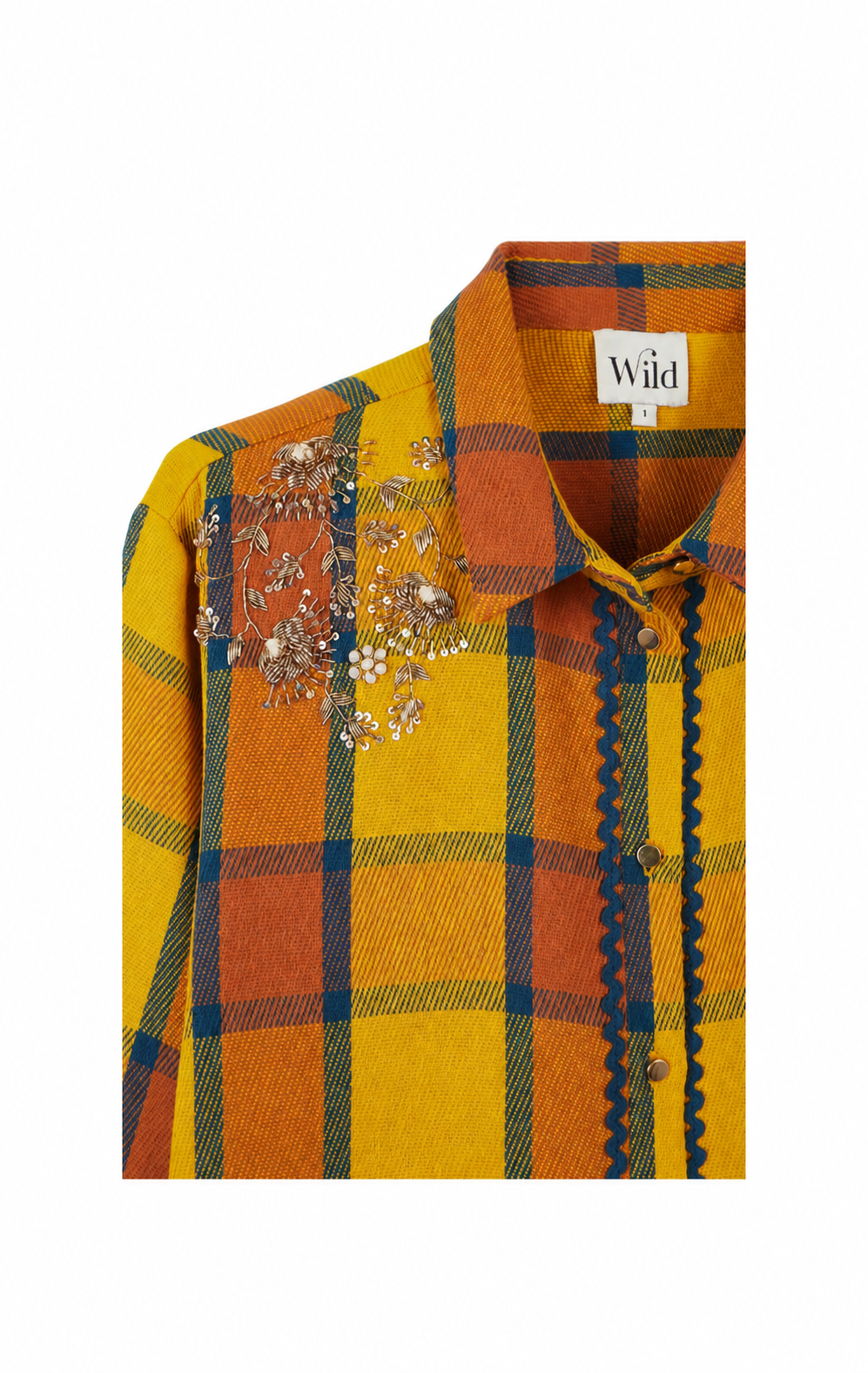 A close-up of a plaid button-up shirt by Wild, featuring a mustard yellow and orange pattern with navy blue lines, scalloped edges, and floral bead embellishments on the chest.