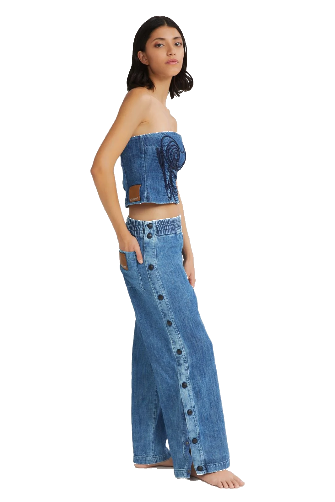 A model wearing a two-piece blue denim set consisting of a strapless cropped top with a spiral graphic and matching wide-leg button-front pants, shown against a plain white background.