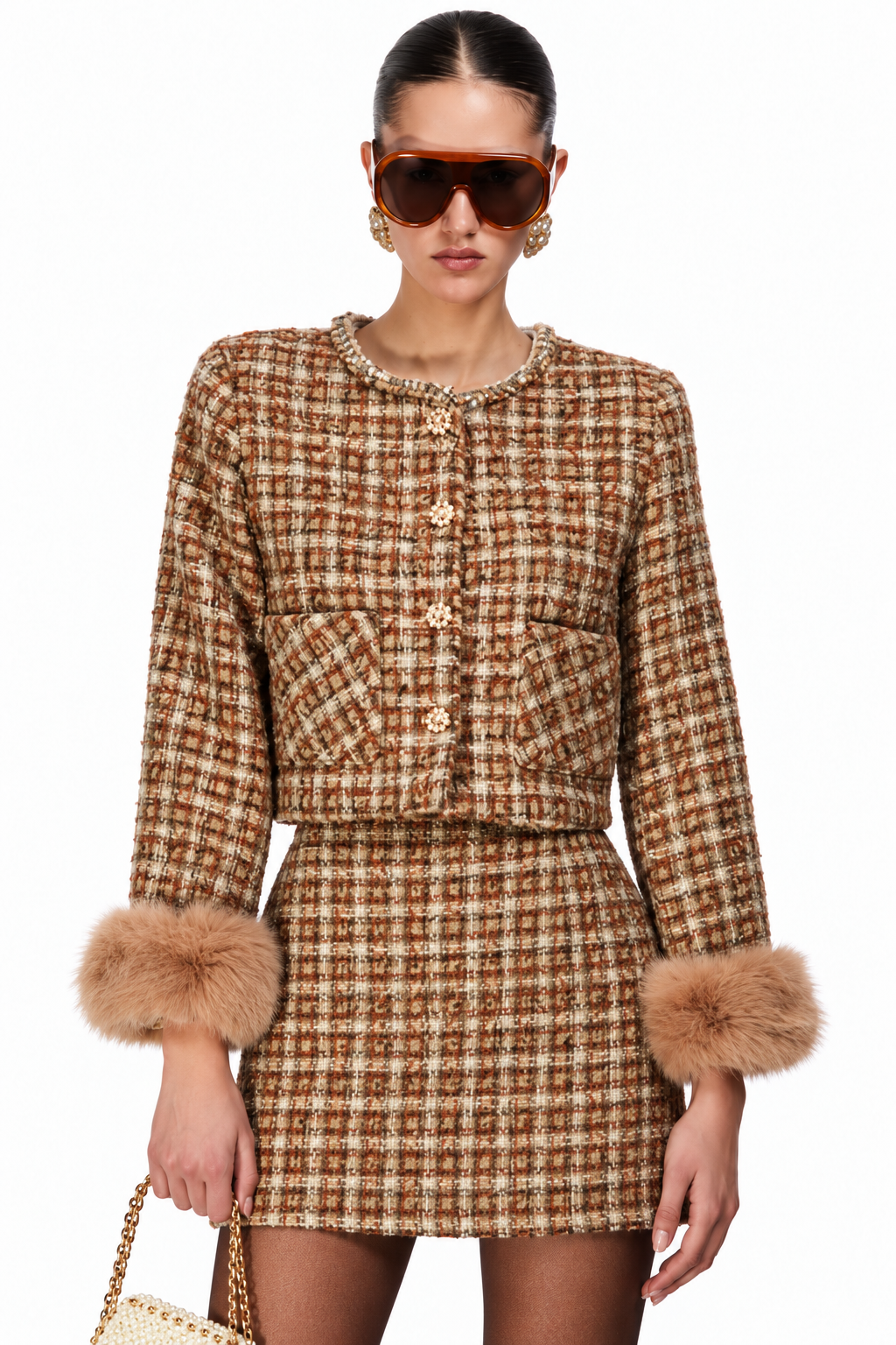 A model wearing a brown and beige tweed mini dress with faux fur cuffs and gold-tone buttons, styled with oversized sunglasses and holding a woven handbag against a plain white background.
