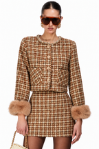 A model wearing a brown and beige tweed mini dress with faux fur cuffs and gold-tone buttons, styled with oversized sunglasses and holding a woven handbag against a plain white background.
