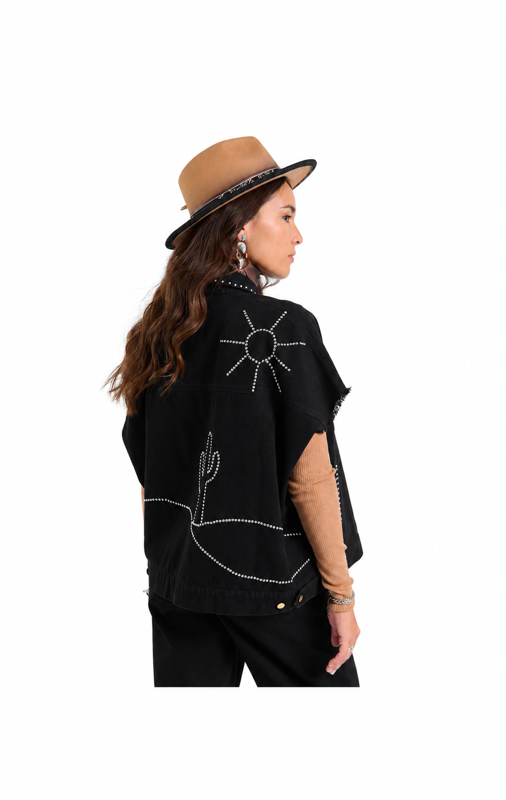 A woman shown from the back wearing a black poncho-style top with white embroidered desert motifs, a tan hat, and black pants against a plain white background.