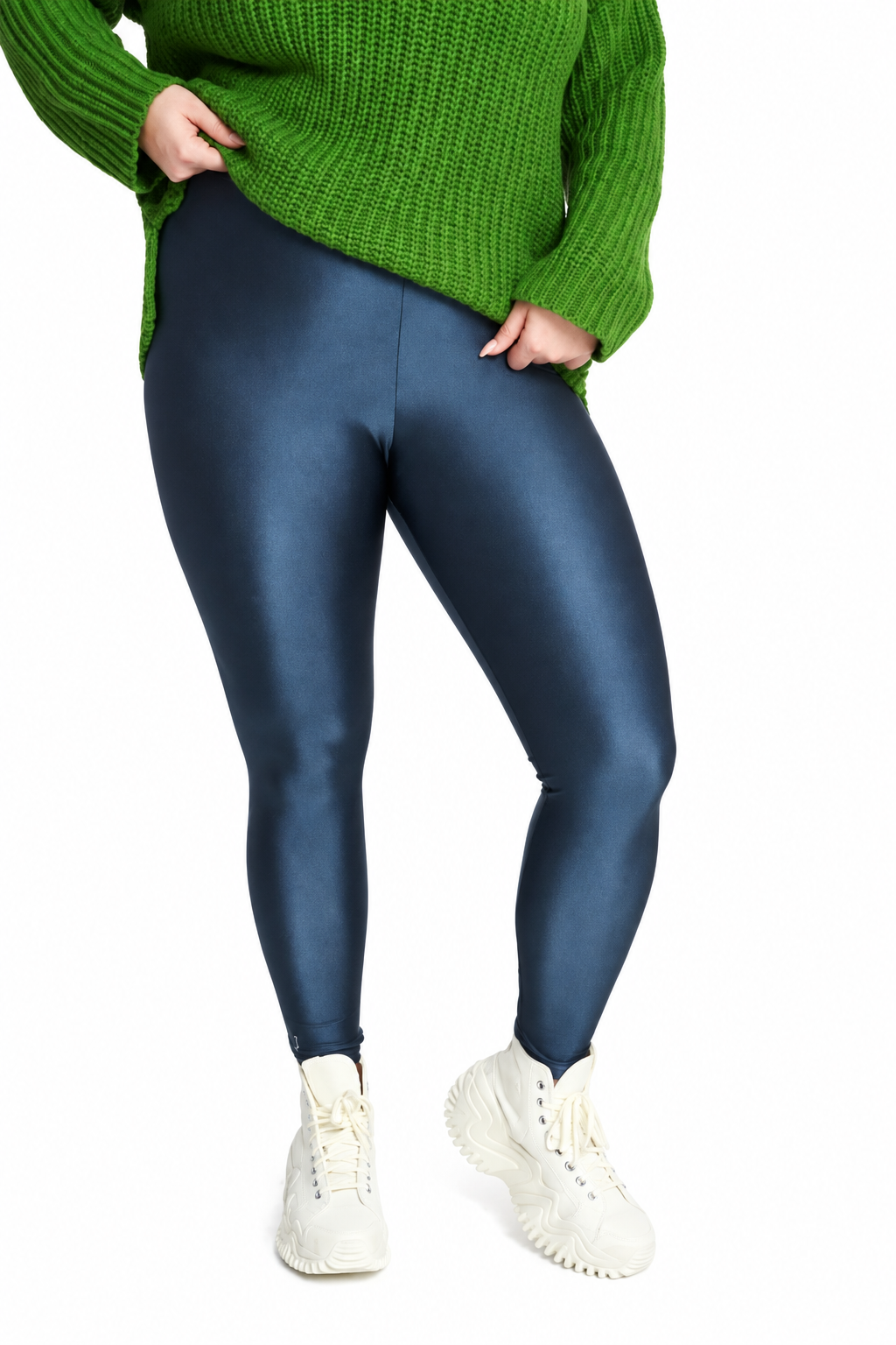 A person wearing shiny dark blue leggings, a green knit sweater, and white sneakers, cropped from the chest down against a plain white background.