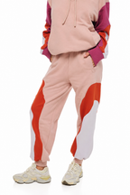 A person wearing a color-blocked hoodie and jogger sweatpants set in pastel pink, orange-red, and white, paired with chunky cream sneakers, against a plain white background.