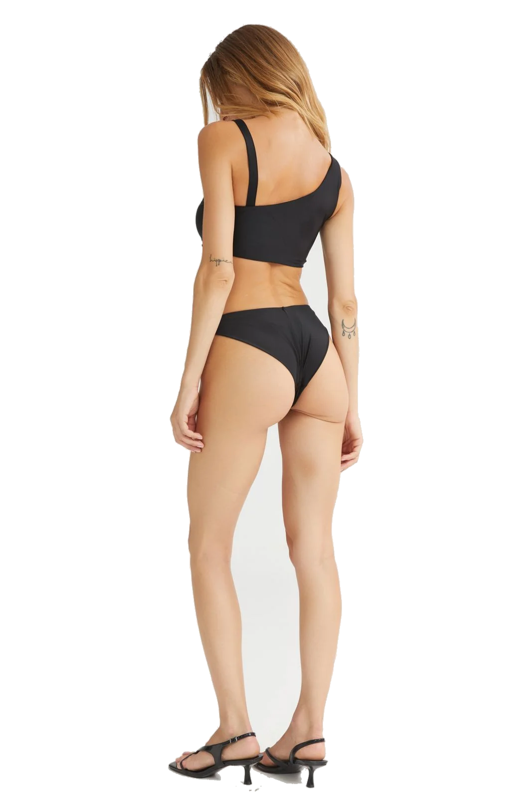 A woman shown from the back wearing a black two-piece bikini with a one-shoulder top and high-cut bottoms, paired with black strappy high-heeled sandals, against a plain white background.