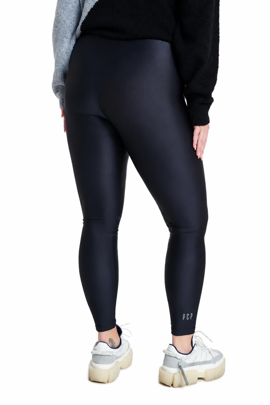 A person shown from the back wearing black high-waisted leggings, a black sweater, and white sneakers against a plain white studio background.