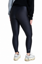 A person shown from the back wearing black high-waisted leggings, a black sweater, and white sneakers against a plain white studio background.