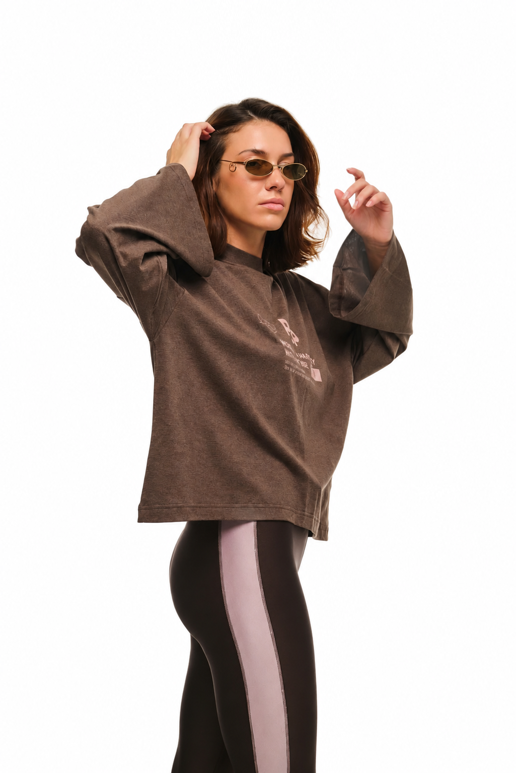 A woman modeling a brown cropped long-sleeve t-shirt with a small graphic print on the left chest, paired with black and white side-striped leggings, against a solid white background.