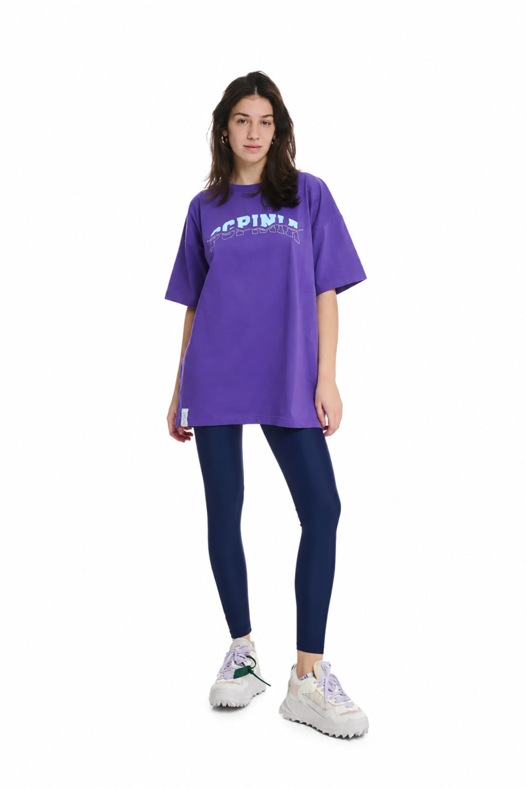 A model wearing a purple oversized t-shirt with 'PCPINIA' printed in light blue across the chest, paired with dark blue leggings and white sneakers, set against a plain white background.