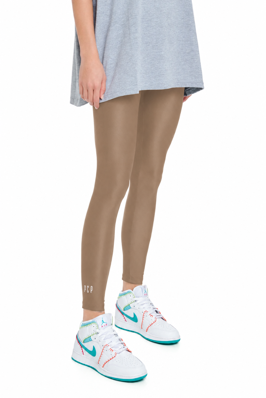 A model's lower body wearing beige leggings, a light gray t-shirt, and white Nike sneakers with teal and orange accents, shown against a plain white background.