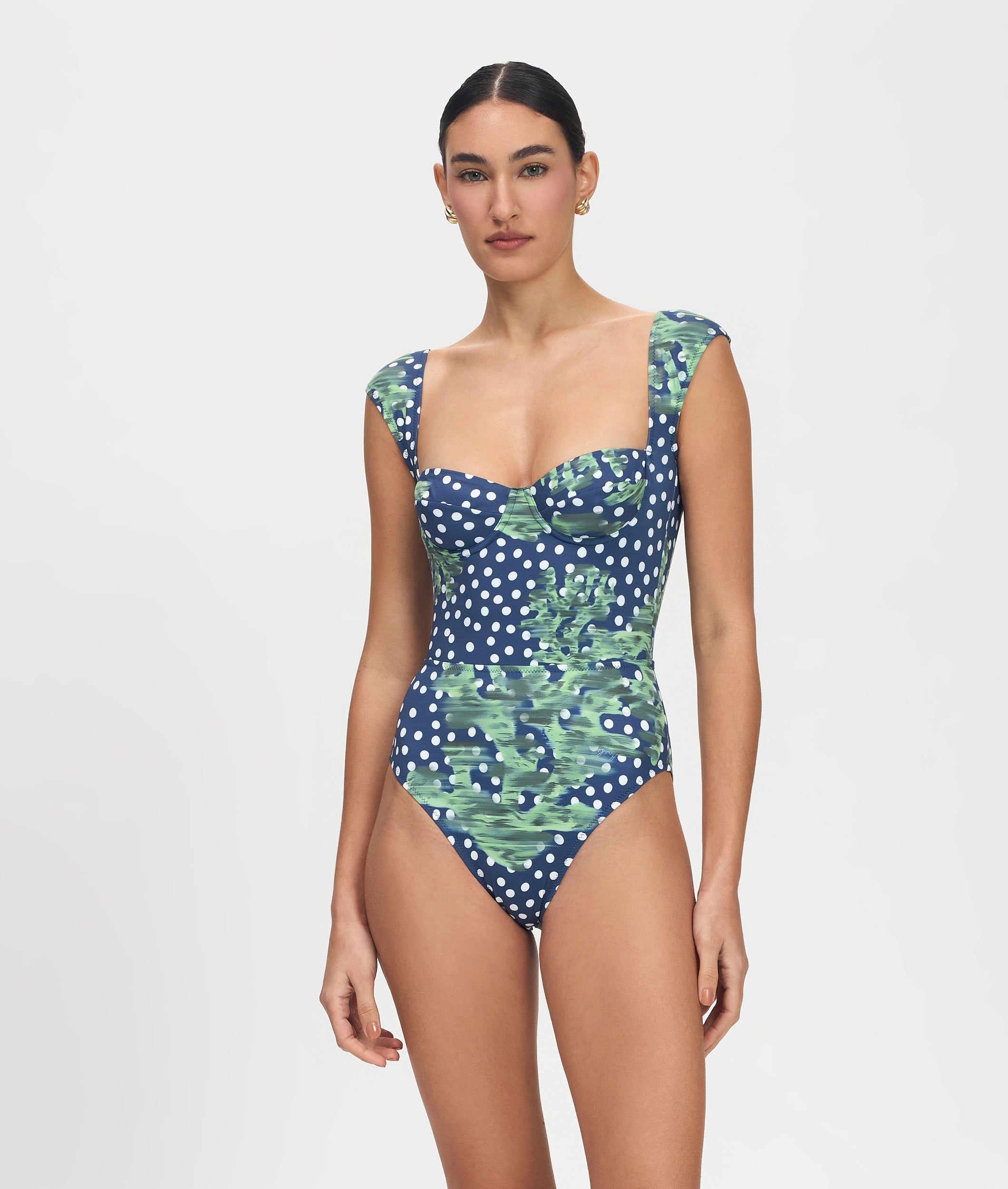 Woman wearing a blue polka dot swimsuit with green leaf pattern on a white background