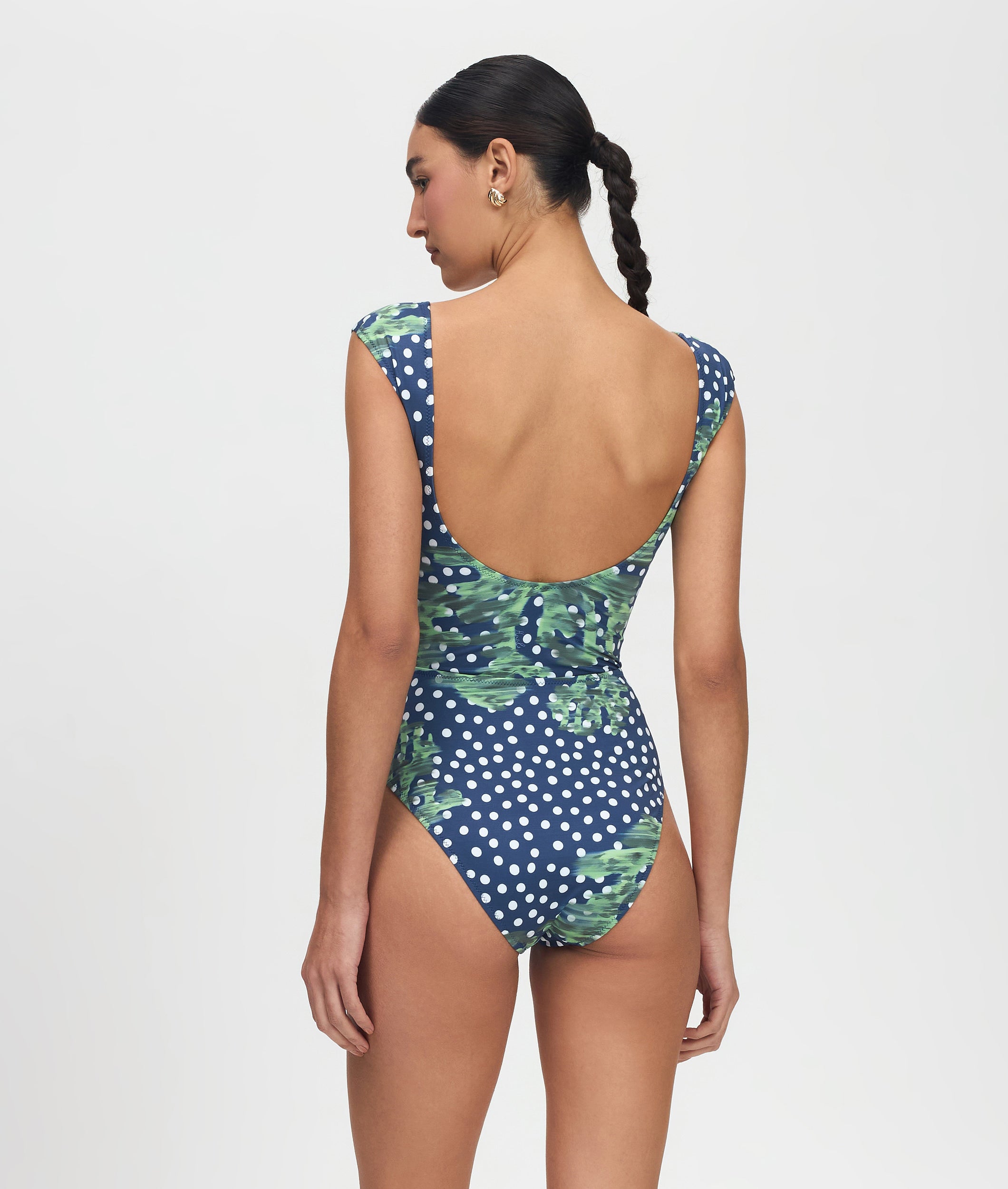 Woman wearing a blue polka dot swimsuit with green leaf pattern on a white background