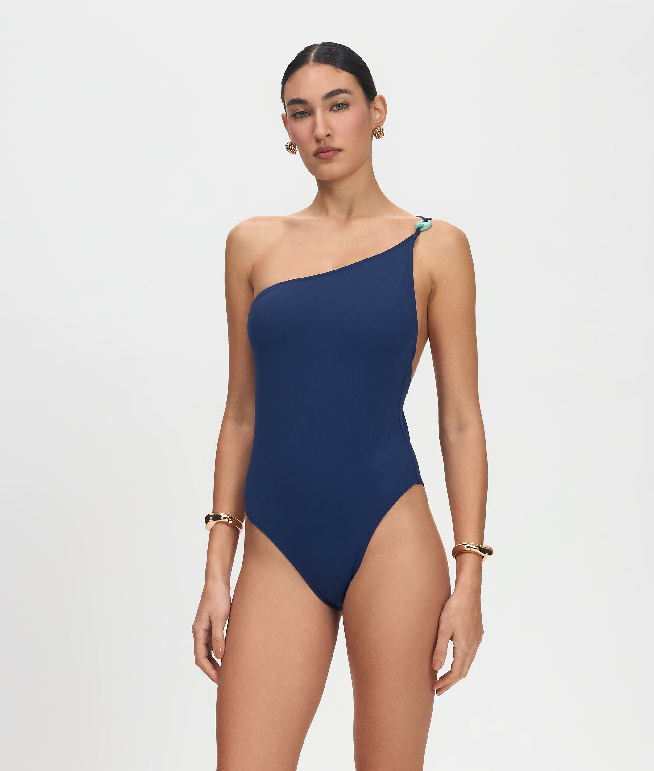 Woman wearing a navy blue one-shoulder swimsuit on a light gray background