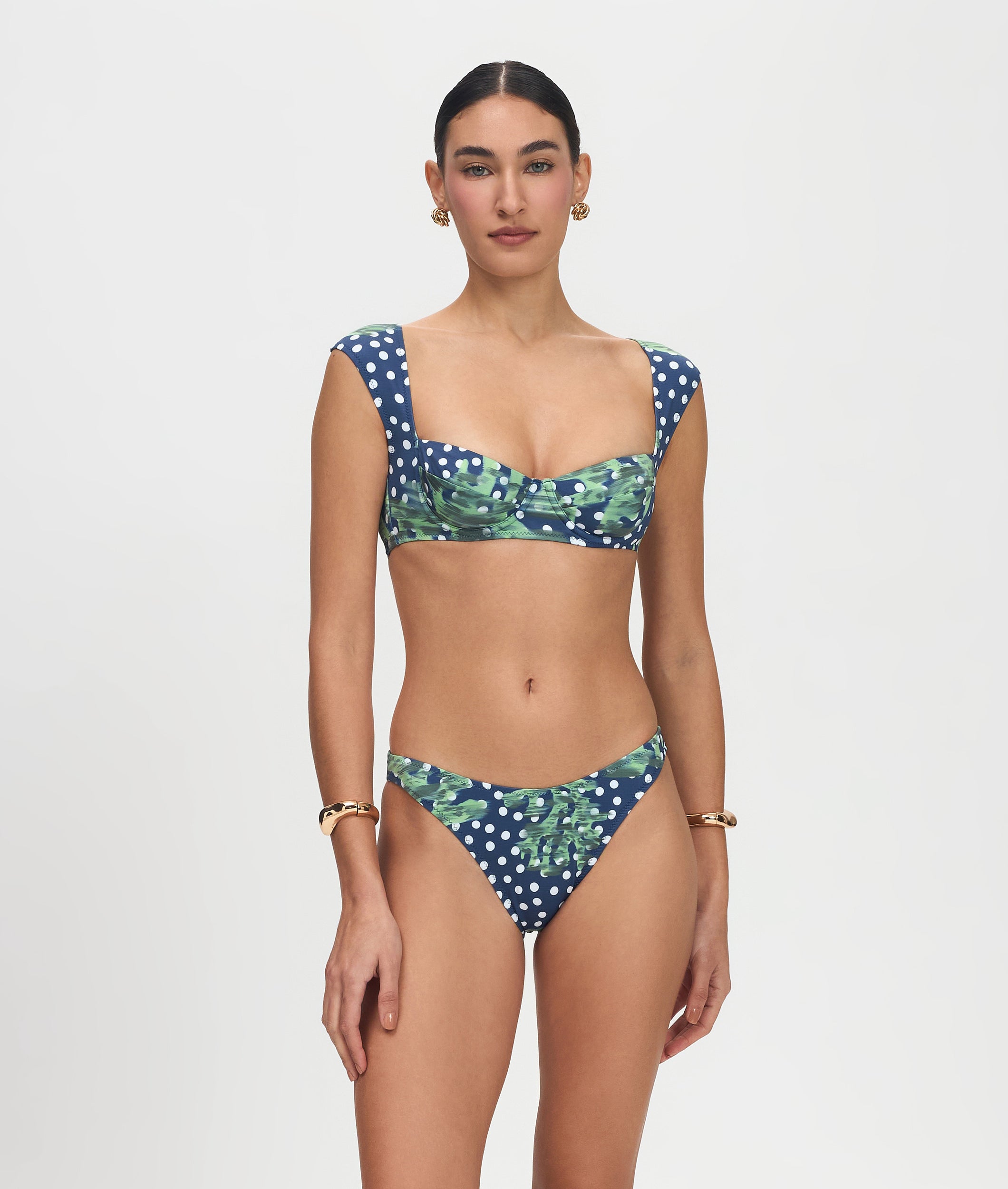 Woman wearing a navy blue bikini with white polka dots and green leaf patterns on a light gray background