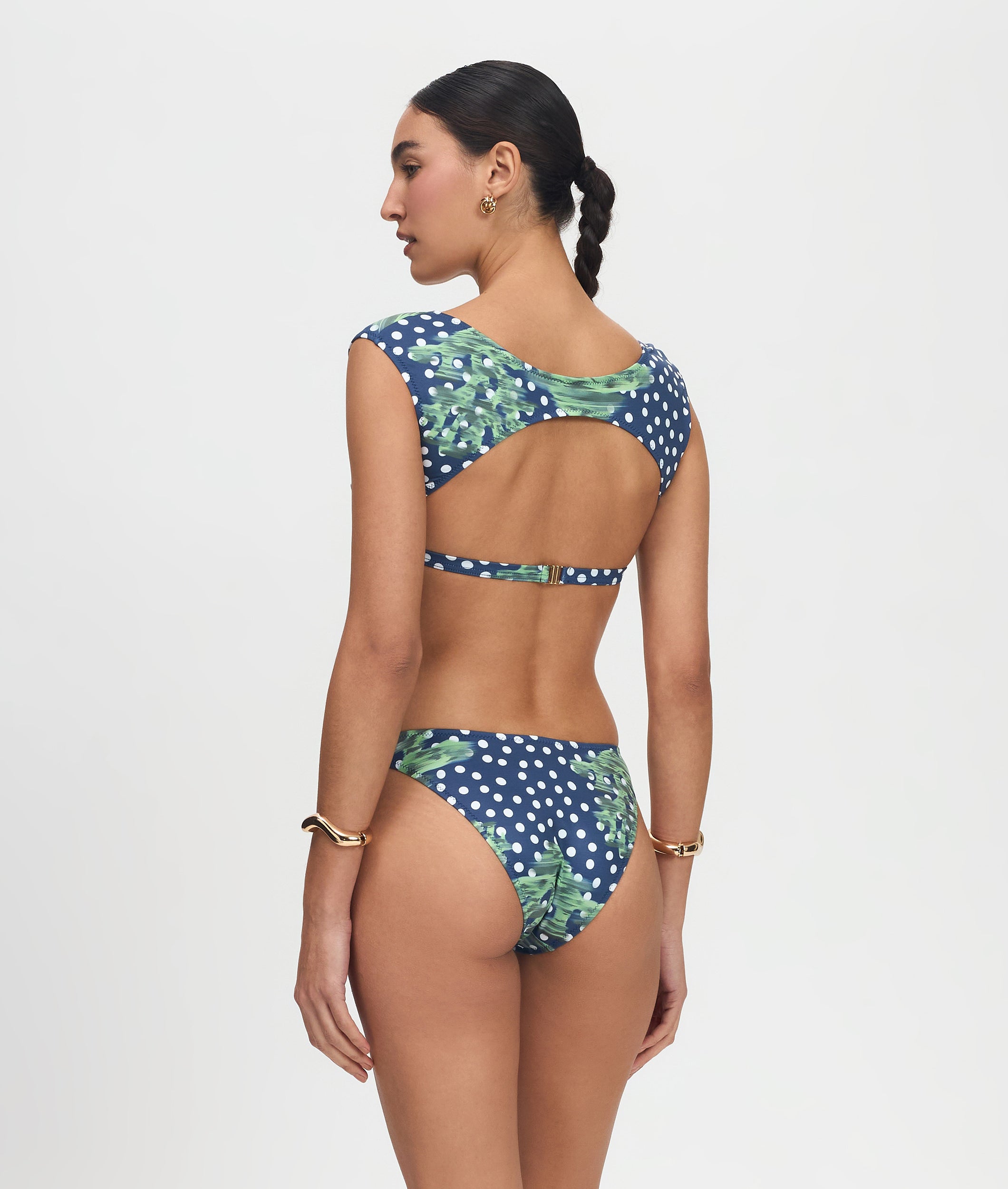 Woman wearing a blue polka dot bikini with green leaf patterns on a white background