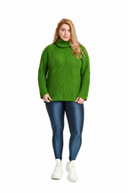 A woman modeling a bright green ribbed turtleneck sweater, paired with dark blue leggings and white sneakers, against a plain white background.