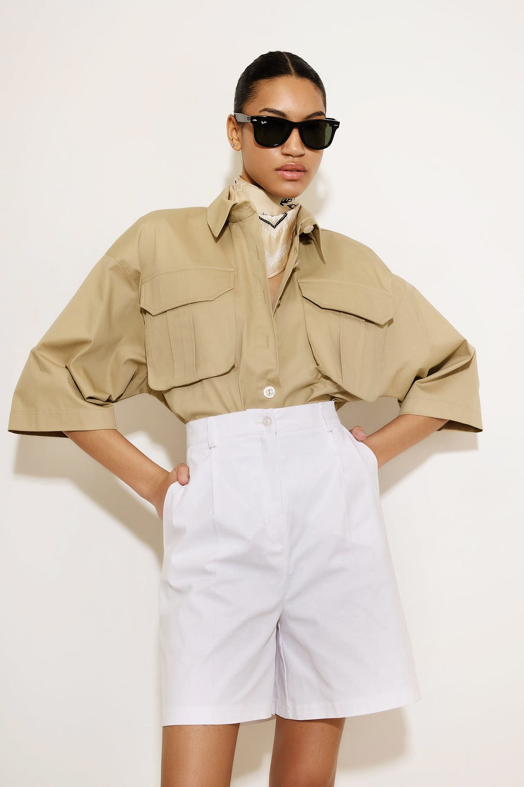 Person wearing a beige jacket and white shorts on a plain background