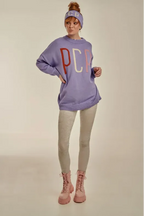 Person wearing a purple sweatshirt with 'PCP' on it, beige leggings, and pink boots against a neutral background.