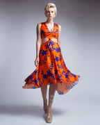 Woman wearing an orange dress with blue floral pattern on a gray background