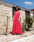 Woman in a red dress standing in front of a stone building with cacti and plants.