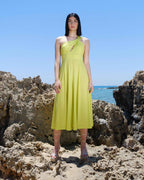 Woman in a yellow dress standing on rocky beach with clear blue sky