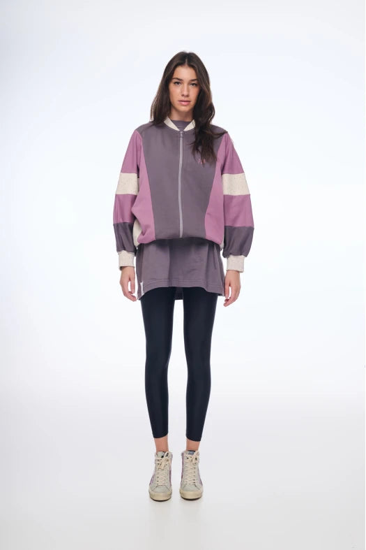Person wearing a purple and pink jacket with black leggings on a white background