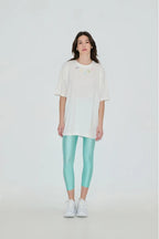 Person wearing a white oversized t-shirt and light blue leggings on a plain background