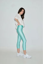 Woman wearing light blue leggings and a white top on a plain background