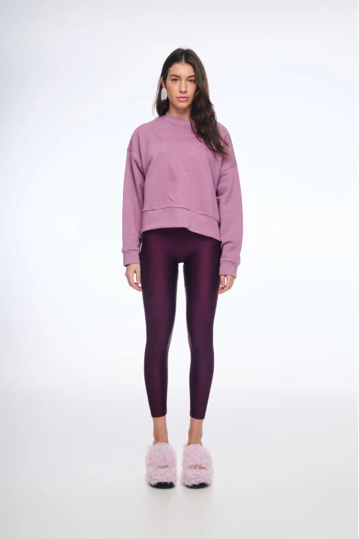 Person wearing a pink sweatshirt and purple leggings on a white background