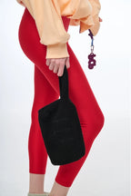 Person wearing red leggings and a beige top holding a black bag on a white background