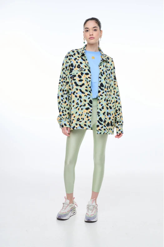 Person wearing a patterned jacket, light blue shirt, green leggings, and white sneakers on a white background
