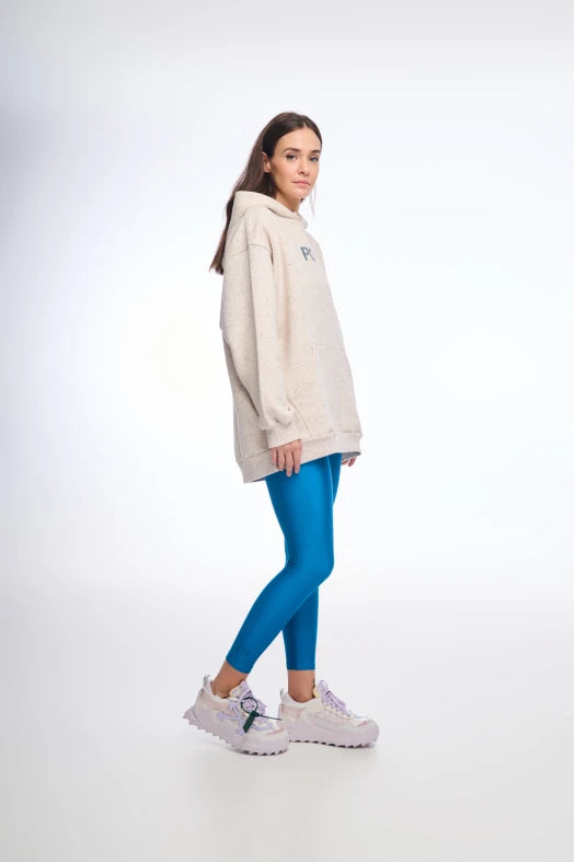 Person wearing a beige hoodie, blue leggings, and white sneakers on a white background