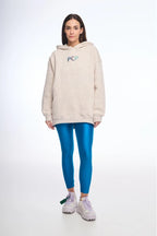 Person wearing a beige hoodie with a logo and blue leggings on a white background