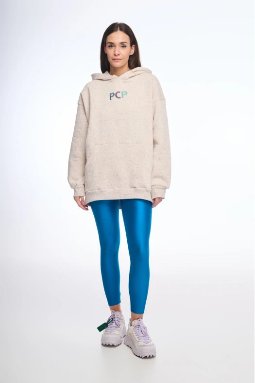Person wearing a beige hoodie with a logo and blue leggings on a white background