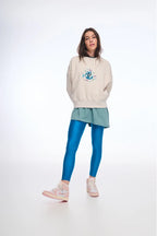 Person wearing a beige sweater with a graphic design, light blue skirt, and blue leggings on a white background