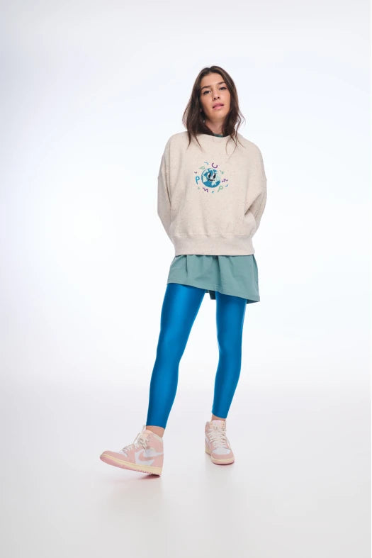 Person wearing a beige sweater with a graphic design, light blue skirt, and blue leggings on a white background